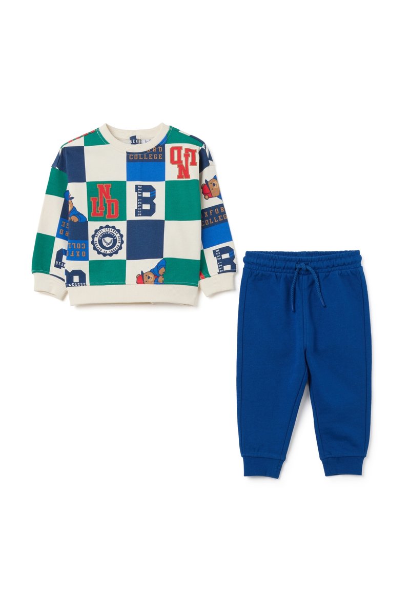 Sweat-shirt avec un motif de damier multicolore comportant des lettres et un graphique d'ours, associé à un pantalon de jogging bleu à taille élastique.