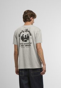 Tricou din bumbac gri, cu un design grafic pe spate, textul spune "Afacerea Familiei" cu trei figuri și detalii de contact tipărite mai jos.