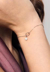 Srebrna bransoletka z delikatnym łańcuszkiem, ozdobiona małym, białym kwiatkiem i okrągłym akcentem.