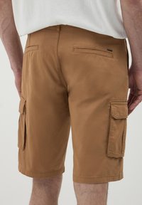 Shorts cargo mi-mollet en tissu marron, dotés de poches latérales, de coutures minimales et d'une texture lisse, avec une poche arrière sécurisée.