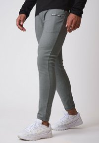 Grå tapered joggers lavet af tekstureret stof, med et lille sort logo-patch. Parret med hvide sportssko.