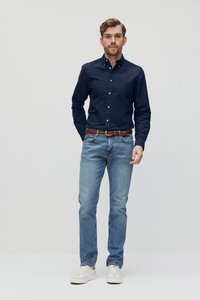 Marineblauw overhemd met knopen, lichtblauwe jeans, bruin gevlochten riem, witte sneakers. Eenvoudig ontwerp, zachte textuur en casual pasvorm.