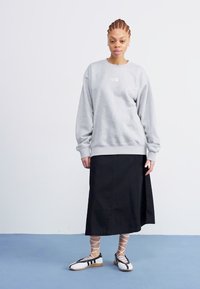 Šedá mikina s manžetami, černá sukně po kotníky a černo-bílé šněrovací boty. Jednoduchý design a měkká textura látky.