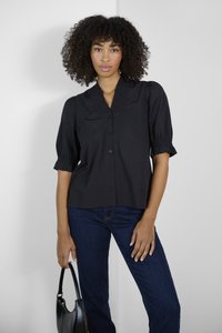 Zwarte blouse met korte mouwen en een ontspannen pasvorm, voorzien van een gerimpelde kraag en knopen aan de voorkant. Gekocht met donkerblauwe jeans en een zwarte tas.