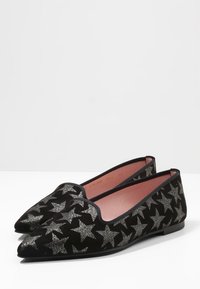 Zapatillas planas de ante negro con punta puntiaguda, decoradas con patrones de estrellas plateadas sobre el material. El interior cuenta con un forro rosa para contraste.