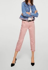 Chaqueta de mezclilla azul claro con un dobladillo floral, camiseta blanca, jeans rosa cortos y zapatos de tacón negros. Conjunto casual con colores distintos.