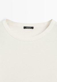 Cremefarvet bomulds-T-shirt med rund hals; har et sort mærke med teksten "Massimo Dutti" nær kraven. Blød tekstur.