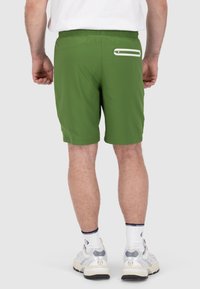 Pantaloni corti sportivi verdi con vita elastica, caratterizzati da una tasca con cerniera bianca sul retro destro e una texture liscia e leggera.