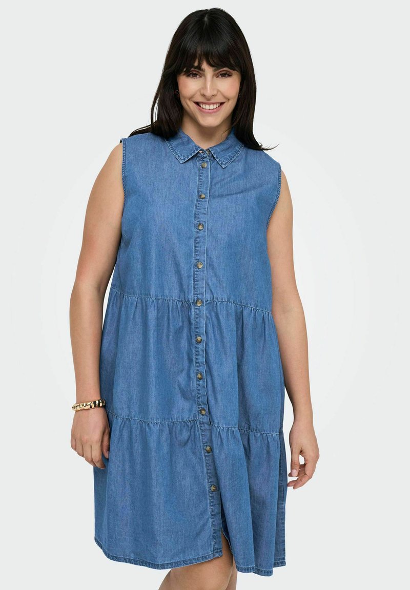 Denim suknelė su apykakle, be rankovių, sluoksniuota volanų apačia ir priekiniais mygtukais užsegama. Šviesiai mėlyna spalva ir švelni tekstūra.