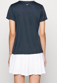 Černé sportovní tričko s krátkými rukávy a bílým límcem, v kombinaci s bílou skládací sukní. Texturovaná tkanina s hladkým povrchem.