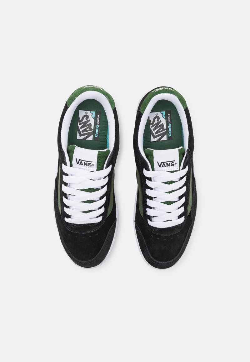 Des baskets Vans noires et vertes en matière suédée, avec des lacets blancs et des semelles intérieures portant la marque. Elles présentent un collier rembourré et une semelle extérieure en caoutchouc texturé.