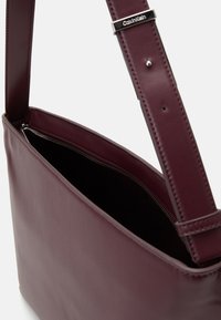 Burgundy leather shoulder bag with a smooth texture, single adjustable strap, and silver zipper detailing on the top opening.