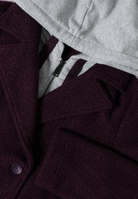Veste en polaire violette avec une capuche grise. Comprend une fermeture éclair sur le devant, des accents en boutons et un tissu texturé pour la chaleur et le confort.