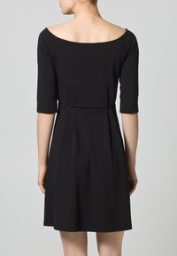 Czarna sukienka z dopasowaną talią, rękawami ¾ i dekoltem odsłaniającym ramiona. Gładki materiał oraz rozkloszowany dół sięgający do połowy uda.