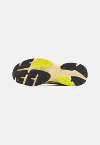 La semelle de chaussure présente des bandelettes en caoutchouc noir avec un motif texturé, des accents jaunes, et une base couleur crème pour une meilleure adhérence.