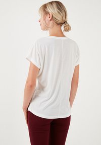 Witte T-shirt met korte mouwen, een ontspannen pasvorm, ronde zoom en omgeslagen mouwen. De stof lijkt zacht met een gladde textuur.