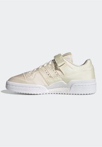 Beige low-top sneaker featuring a smooth texture, strap closure, white sole, and subtle perforations on the side for breathability.