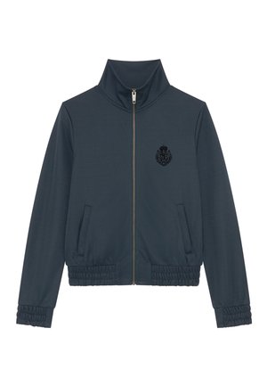 Chaqueta navy con cuello alto, cierre completo, dos bolsillos laterales, puños elásticos y un escudo texturizado negro en el pecho.