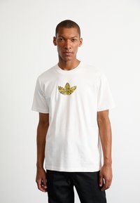 Vit bomull t-shirt med en färgglad, tryckt Adidas-logotyp på bröstet. Klassisk rund halsringning och korta ärmar.