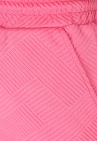 Růžová tkanina s texturovaným vzorem rovnoběžných a diagonálních linek, která ukazuje jemný, elastický materiál a hladký povrch.
