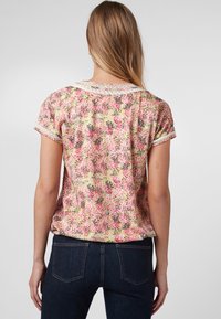 Blusa floral de manga corta con un estampado en tonos rosa, amarillo y verde. Presenta un cuello texturizado y hombros fruncidos. Tejido suave.