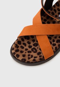 Oransje semsket skinnsandaler med kryssede stropper og en brun leopardmønstrede innersåle. Lav profil såle med teksturert overflate.