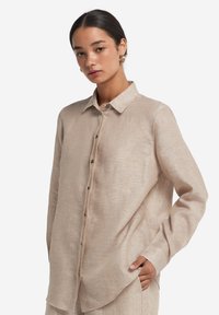 Lys beige linned skjorte med krave, frontknapper og lange ærmer, der har en afslappet pasform og en subtil tekstur.