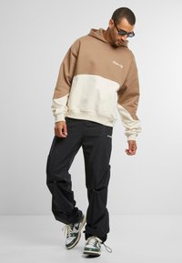 Hettegensere i beige og kremfarge med fargedeling og ribbede mansjetter. Bært med svarte cargobukser og grønne og hvite joggesko.