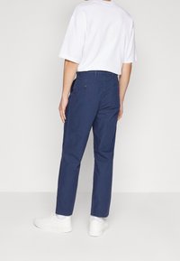 Námořnicky modré bavlněné kalhoty s rovný střih, s zadními kapsami a poutky na opasek, doplněné bílým tričkem a bílými teniskami.