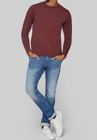 Tummanpunainen pitkähihaispaita, jossa on kurttupinta, yhdistettynä vaaleansinisiin kapealahkeisiin farkkuihin ja valkoisiin lenkkareihin. Rentoa tyyliä, siisti muotoilu.