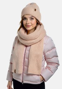 Lyserød strikket hue og tørklædesæt med ribbet struktur. Huens kant er foldet, og tørklædet er bredt og langt.