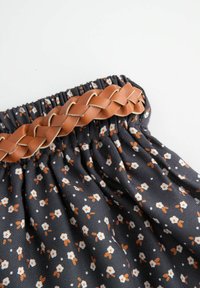 Spódnica z materiału w kwiatowy wzór na ciemnym tle, zdobiona małymi białymi i pomarańczowymi kwiatami oraz warkoczowym paskiem z jasnobrązowej skóry na talii.
