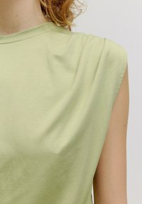 Lichtgroene mouwloze T-shirt gemaakt van zachte katoen. Heeft een relaxte pasvorm met een ronde halslijn en smalle, minimale naden.