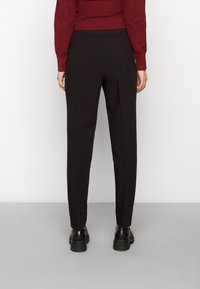 Black tailored trousers with a straight cut and smooth texture. Worn with black chunky shoes. Back view highlights the clean lines and fit.
