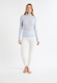 Maglia aderente a maniche lunghe azzurro chiaro con collo alto a costine, abbinata a leggings bianchi, entrambi realizzati in tessuto elasticizzato, su uno sfondo semplice.