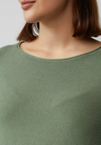 Groene gebreide top met een zachte textuur en een brede halslijn, voorzien van een geribde zoom en raglanmouwen.