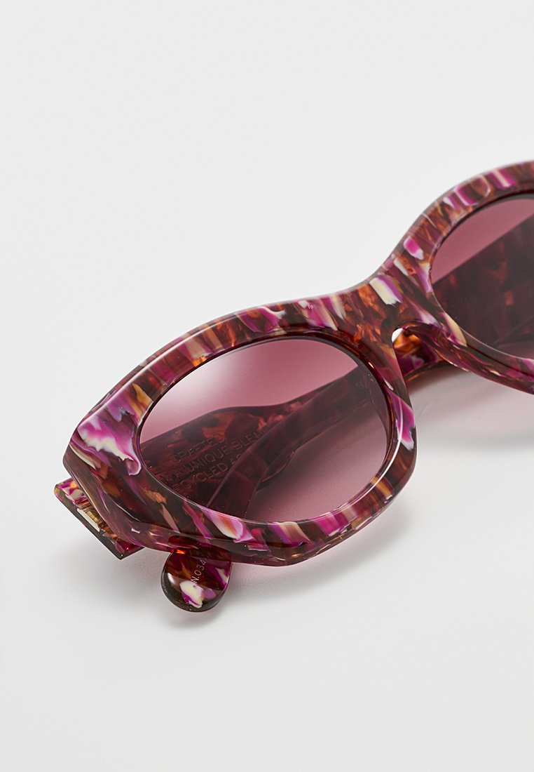 Okulary przeciwsłoneczne z dużymi, okrągłymi ramkami w różowym, fioletowym i brązowym wzorze żółwia oraz zabarwionymi soczewkami, na białym tle.