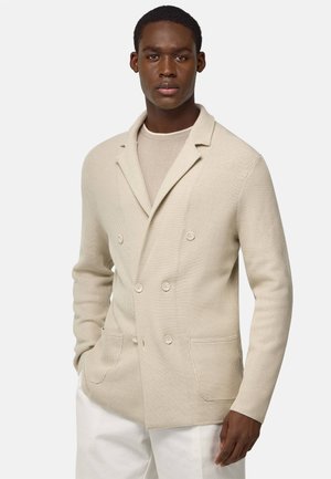 Beige double-breasted blazer with a textured knit fabric, featuring notched lapels, two front pockets, and light-colored buttons.