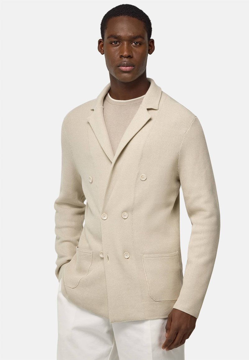 Beige dvojřadový sako s texturovaným pleteným materiálem, má klopové límce, dvě přední kapsy a světlé knoflíky.