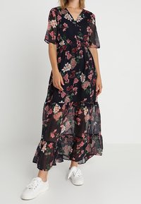 Robe longue à fleurs en bleu marine foncé, confectionnée en tissu transparent avec manches courtes, dotée d'un col en V, d'une taille élastique et d'un détail à volant à l'ourlet.