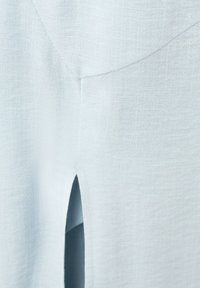 Tissu bleu clair avec une fente verticale centrée et des lignes de couture visibles formant un V en haut de la fente.