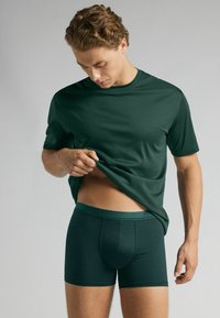 Mörkgrön, åtsittande t-shirt och matchande boxershorts, tillverkade av mjukt tyg med en len yta; korta ärmar och elastisk midja.