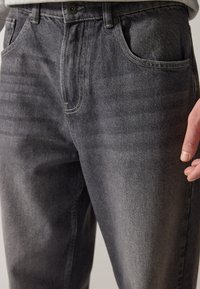 Dark gray denim jeans featuring a straight-leg design, five pockets, and contrasting stitching details. Material is textured with a smooth finish.
