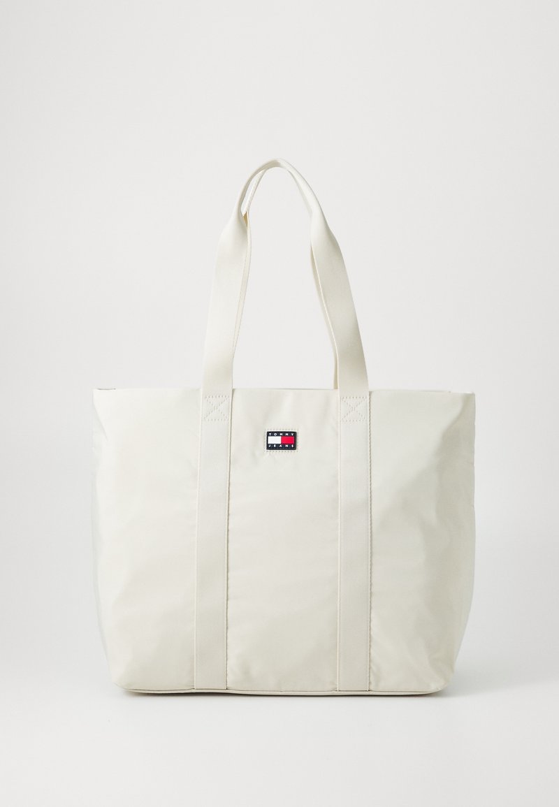 Sac fourre-tout beige en matériau lisse et durable. Il est doté de deux solides bretelles d'épaule et d'une petite étiquette logo au centre.