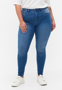 Jeans ajustados de mezclilla azul de cintura alta con una textura suave, que cuentan con lazos para cinturón, bolsillos frontales y cierre de cremallera.