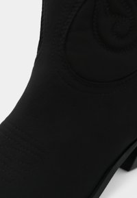 Μαύρο δερμάτινο μπότες με ανάγλυφο σχέδιο στροβίλου και λεπτομερή ραφή στο πέλμα και το πάνω μέρος, πάνω σε λευκό φόντο.