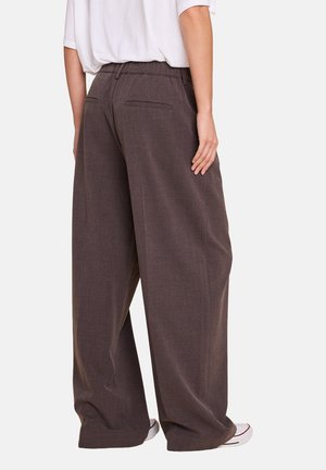 Bredde ben, brune bukser laget av teksturert stoff, med elastisk midjebånd og to baklommer. Brukt med en løs hvit topp.