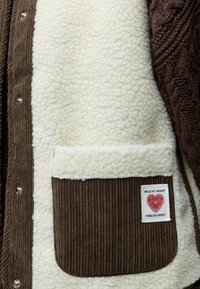 Veste en velours côtelé marron et polaire crème avec poche plaquée étiquetée "Wild at heart, free in spirit" et boutons-pression en métal.