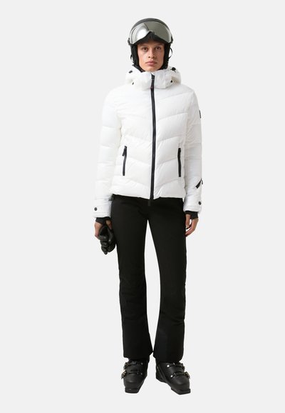 Witte geïsoleerde skijack met een capuchon, ritssluiting en zwarte accenten, gecombineerd met zwarte skibroeken en handschoenen. Model met een helm op.