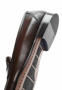 Chaussure en cuir brun avec un bout arrondi et un petit talon. Texture lisse avec des détails cousus et une semelle en caoutchouc texturée.